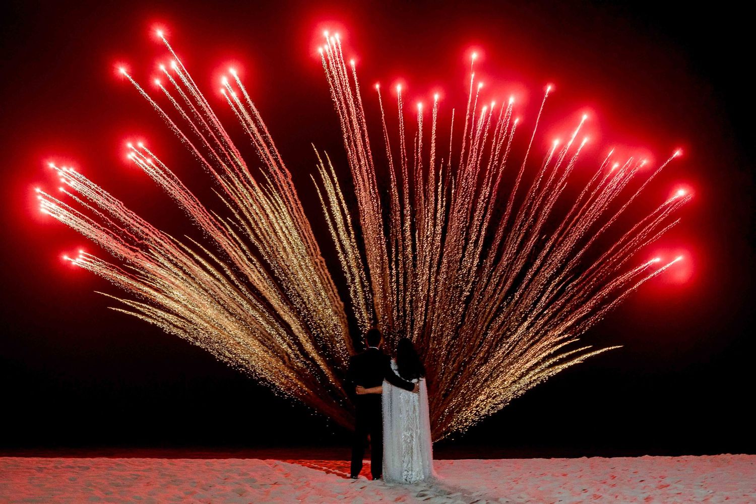 Red fireworks illuminate the night sky in a spectacular display of pyrotechnics over a dark silhouetted landscape.