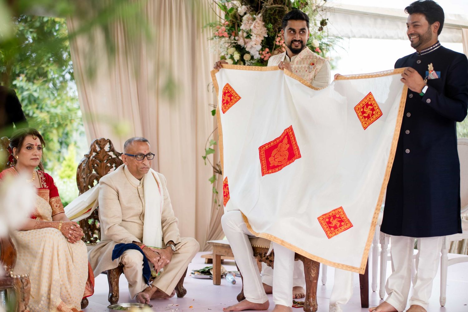 Traditional ceremony participants holding white fabric with red decorative cards.