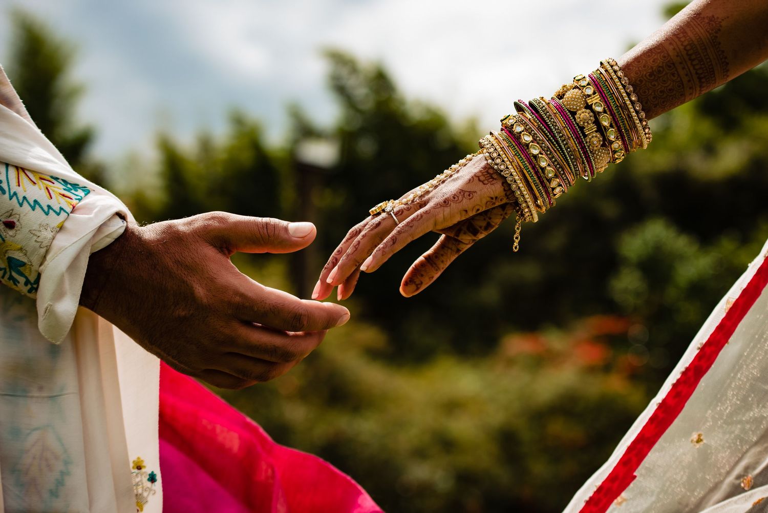Close-up of hands with traditional Indian wedding jewelry and henna designs.