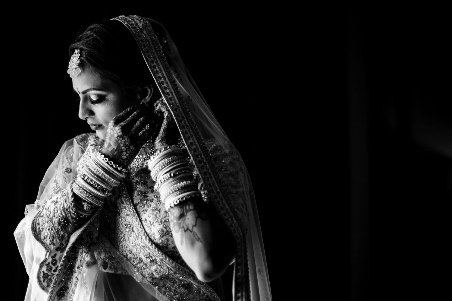 Dramatic black and white portrait of a bride in traditional Indian wedding attire and veil.