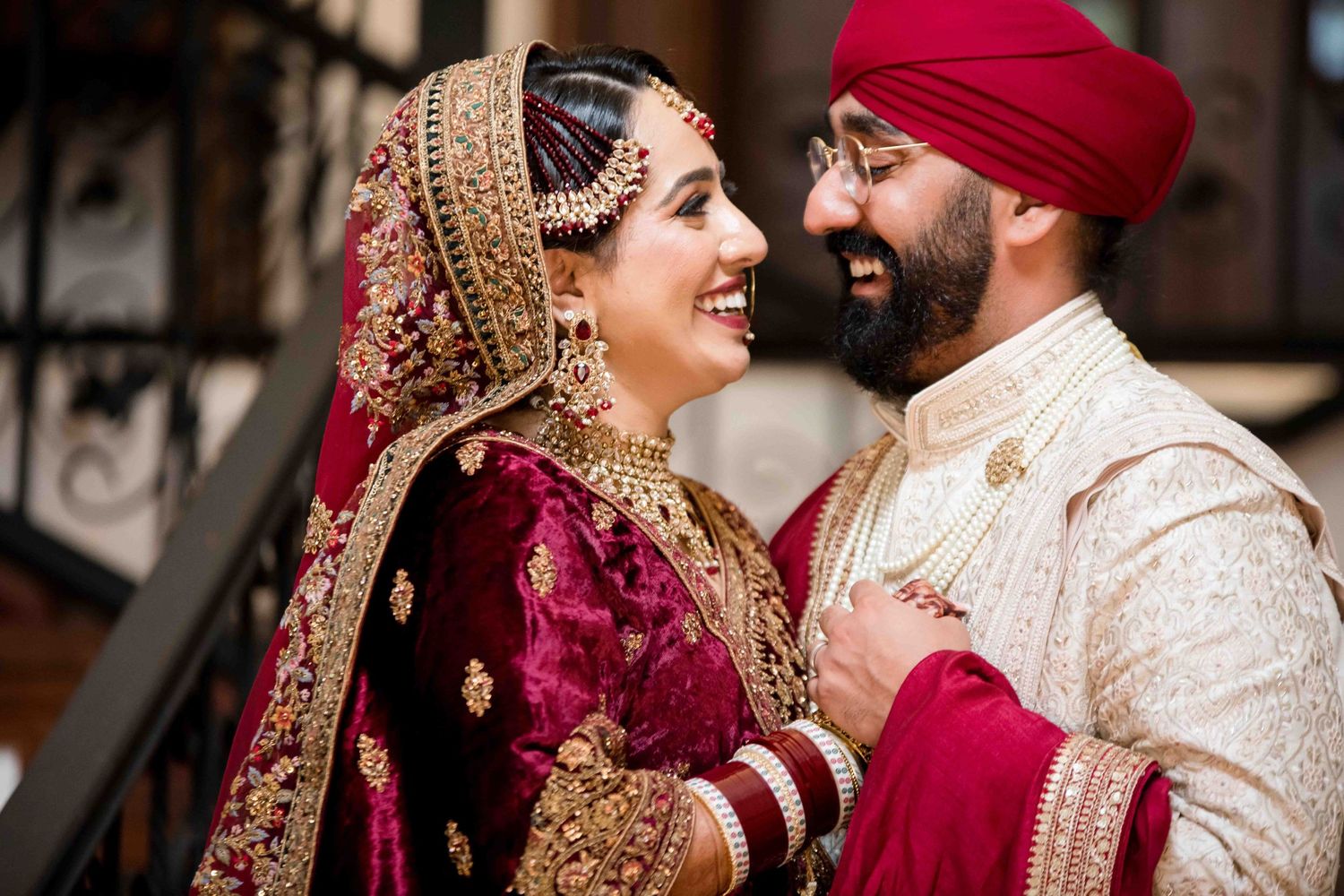 Couple in traditional Sikh wedding attire share intimate moment against architectural backdrop.