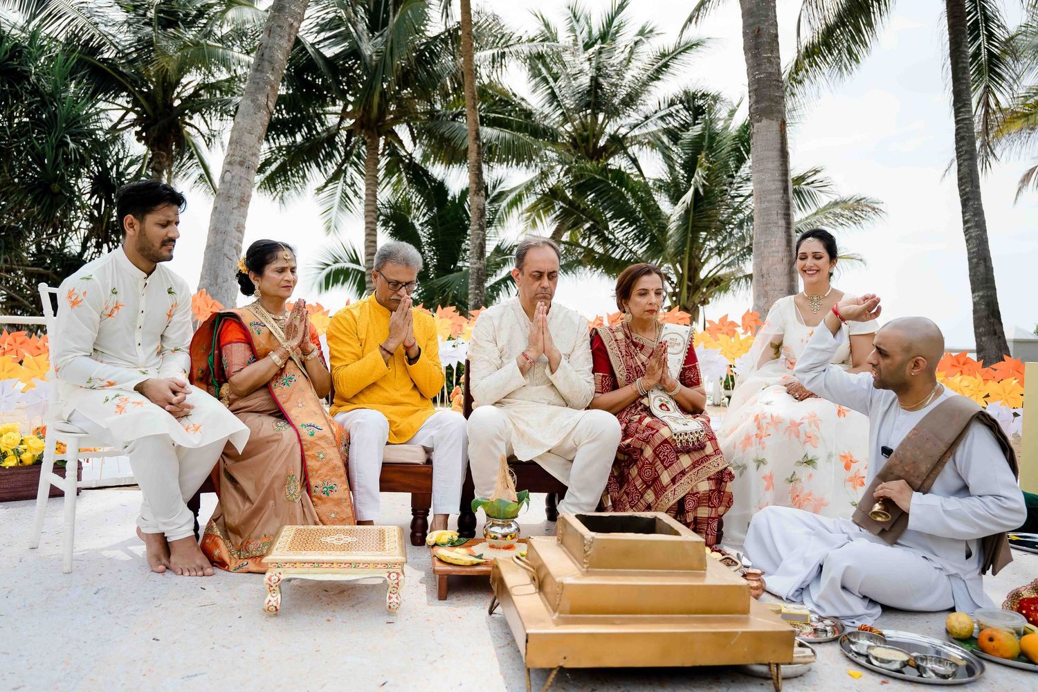 Wedding guests in white attire enjoy a beachside celebration with palm trees and tropical decor.