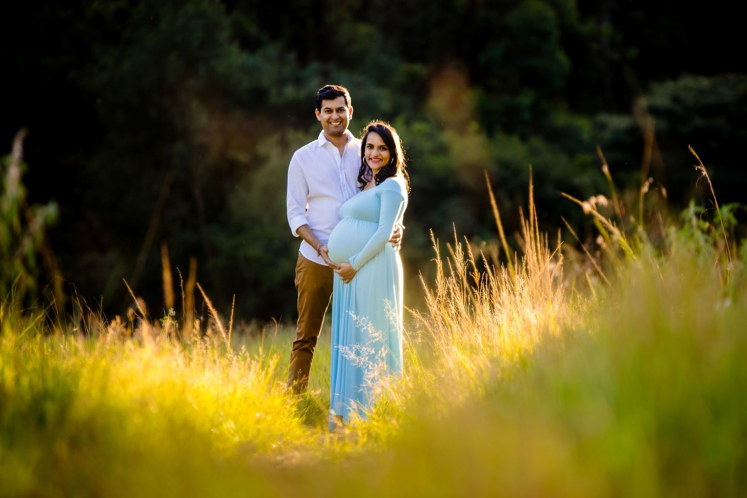 Romantic couple photoshoot in field during golden hour with soft natural lighting.
