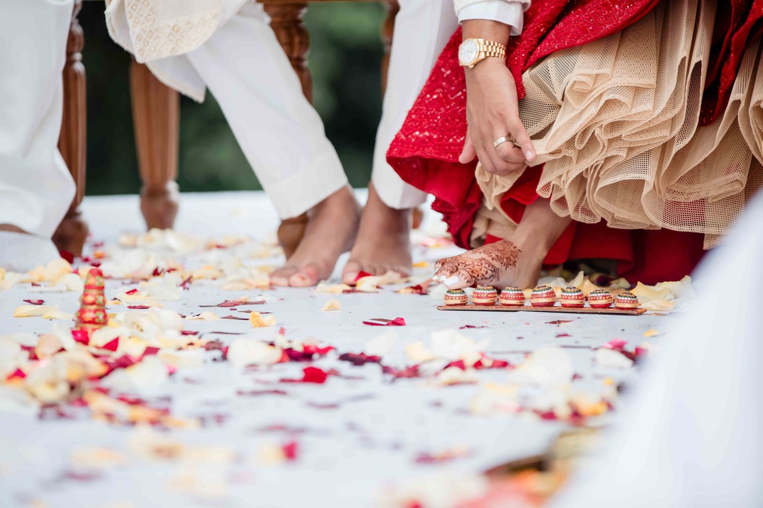 Feet walking on white fabric decorated with scattered red rose petals during a wedding ceremony.