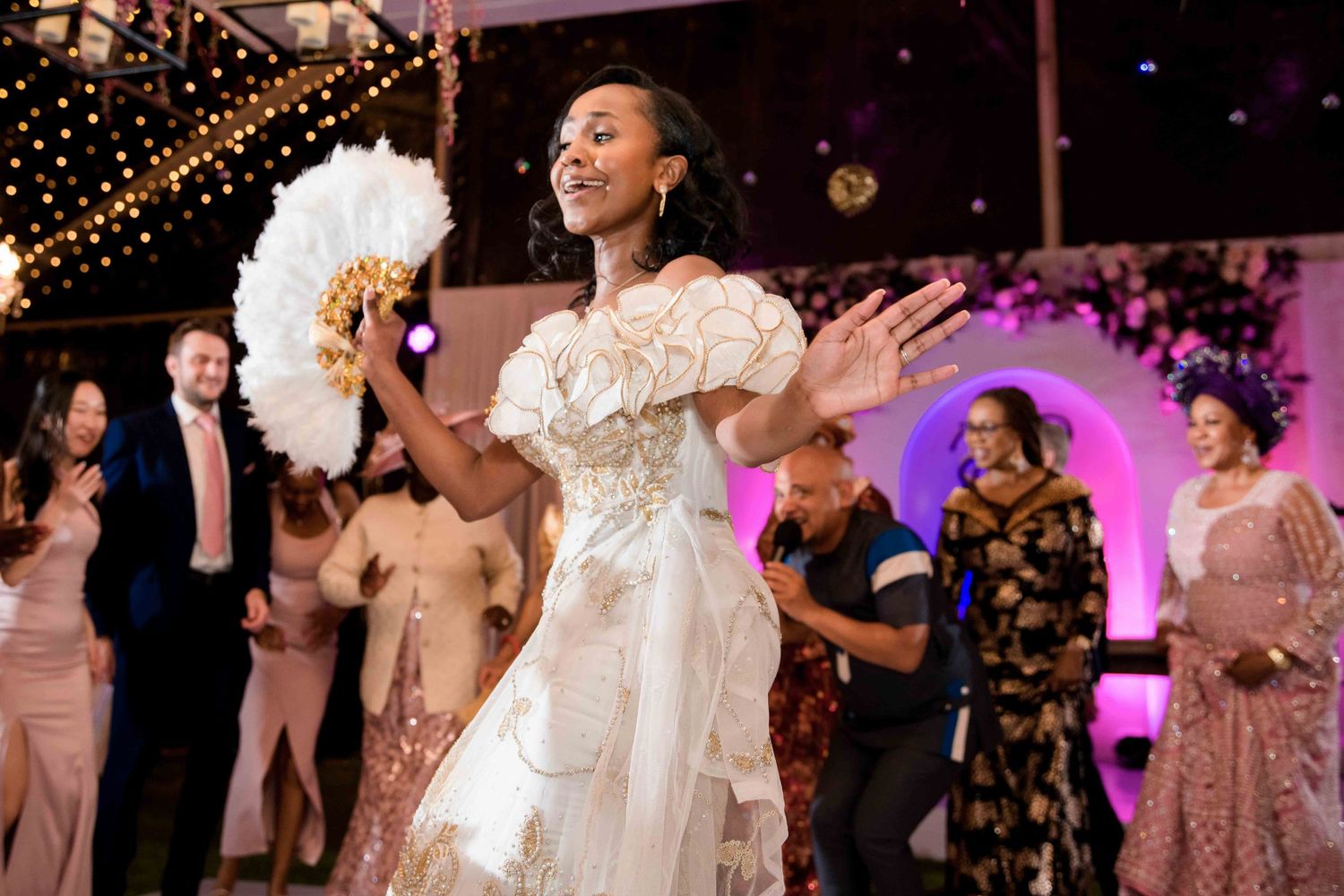A bride dancing energetically at her reception under twinkling lights and purple ambient lighting.