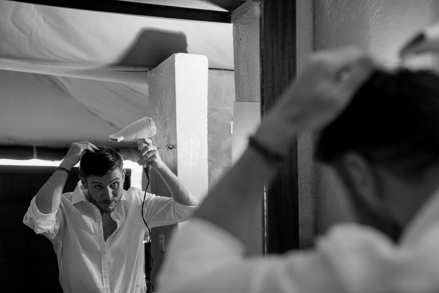 Black and white reflection of a person adjusting their outfit in a mirror.