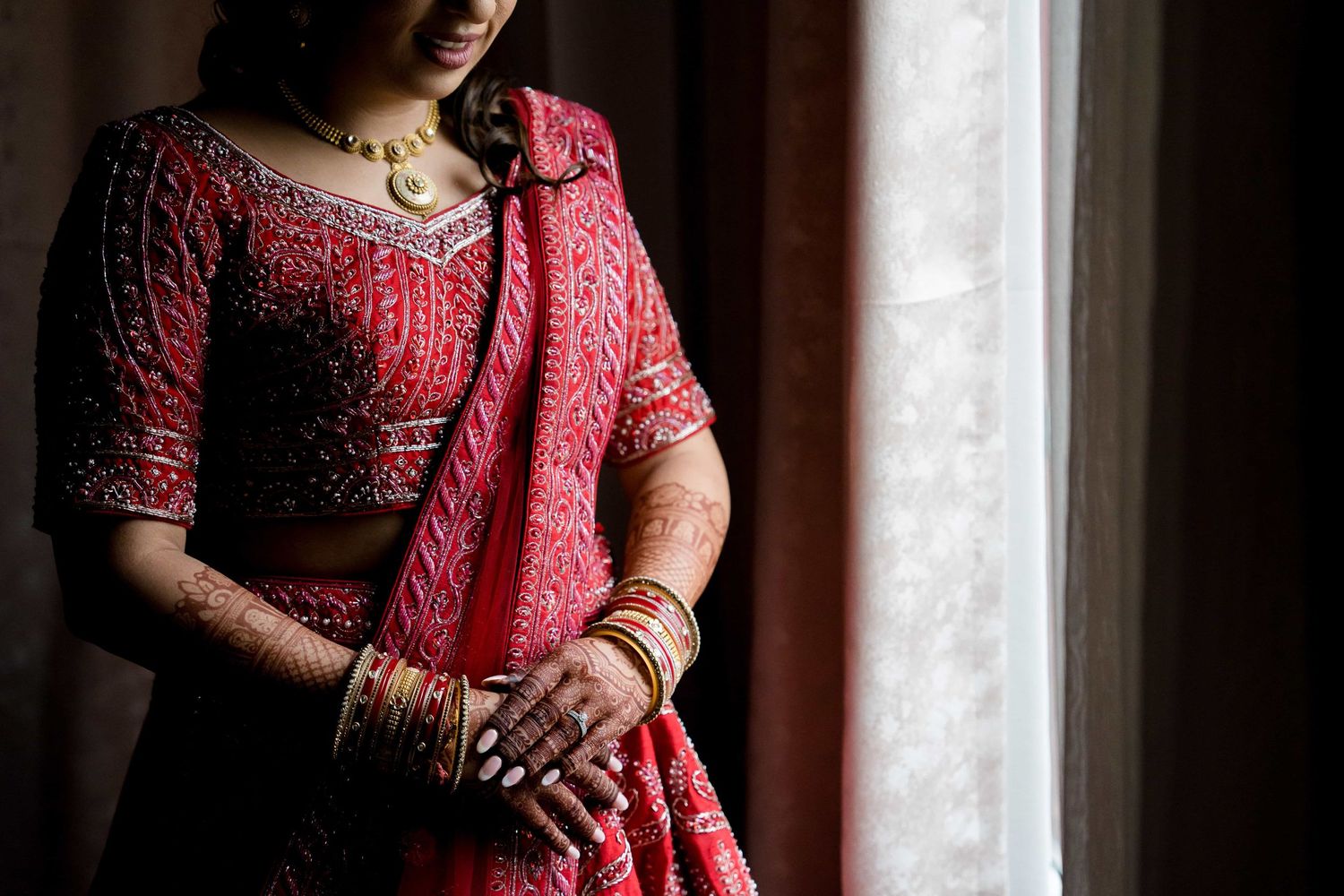 Traditional red bridal lehenga with intricate embroidery captured in window light.