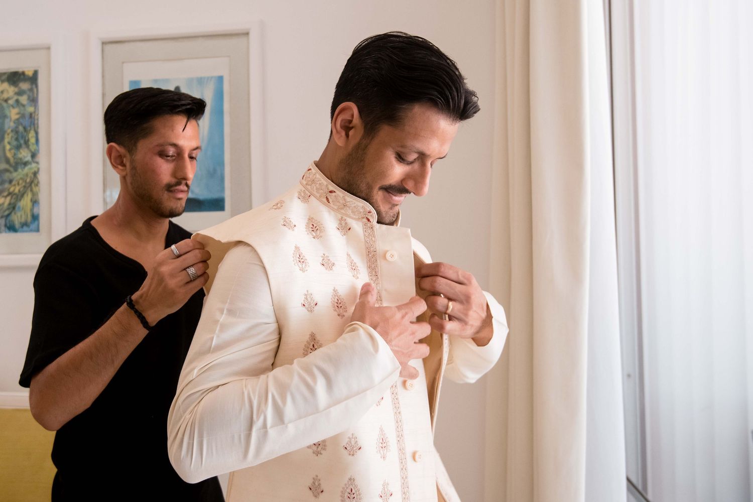Groom getting ready for wedding day in white dress shirt and black bow tie in bright room.