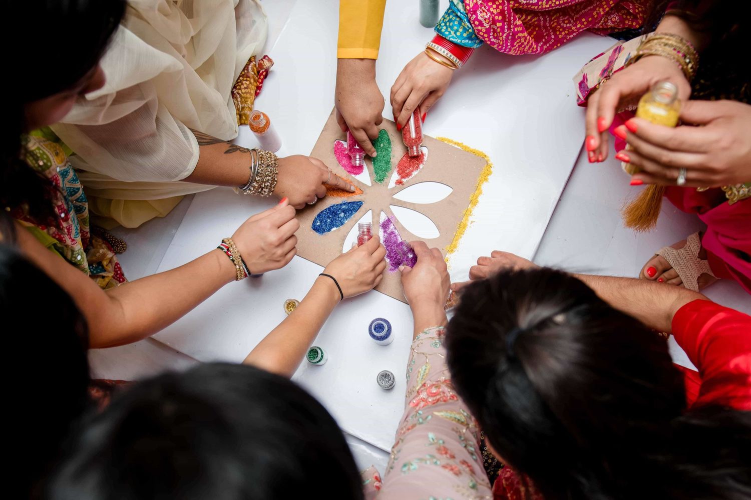 Hands gathered around table decorating and creating traditional Indian wedding art.