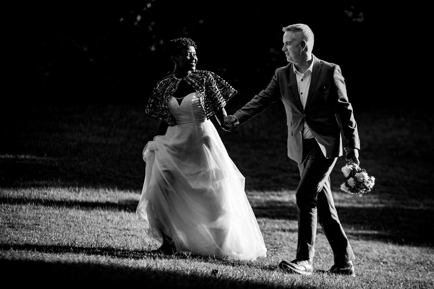 Black and white wedding photography capturing candid moments on a grassy field.