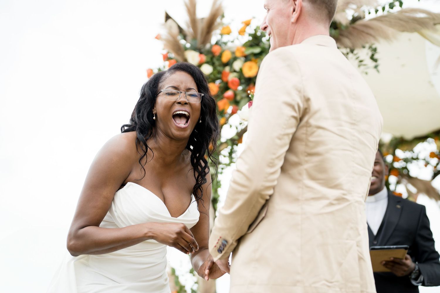 Joyful moment shared during outdoor wedding ceremony beneath floral arch.