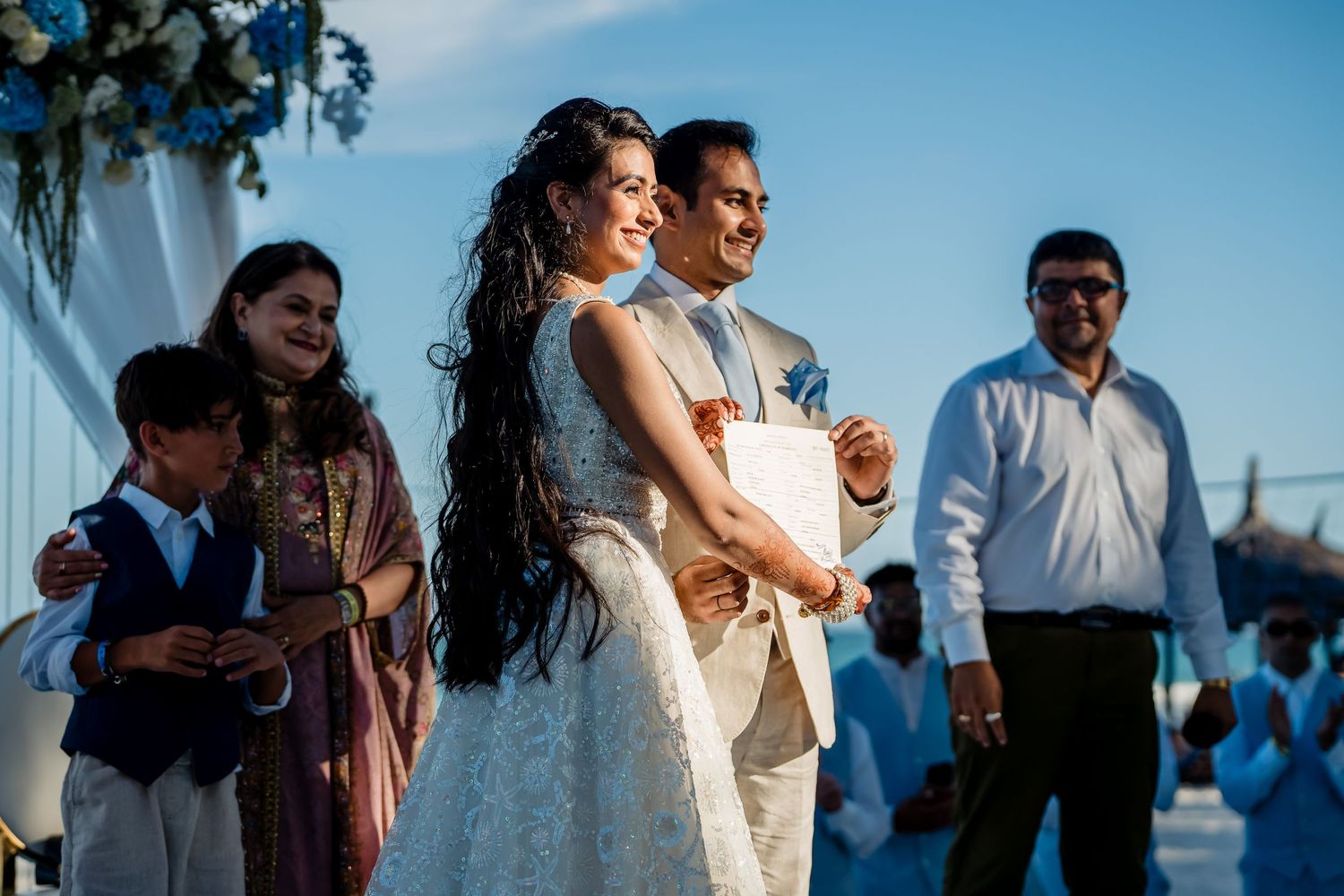 Outdoor beach wedding celebration with blue floral decorations.