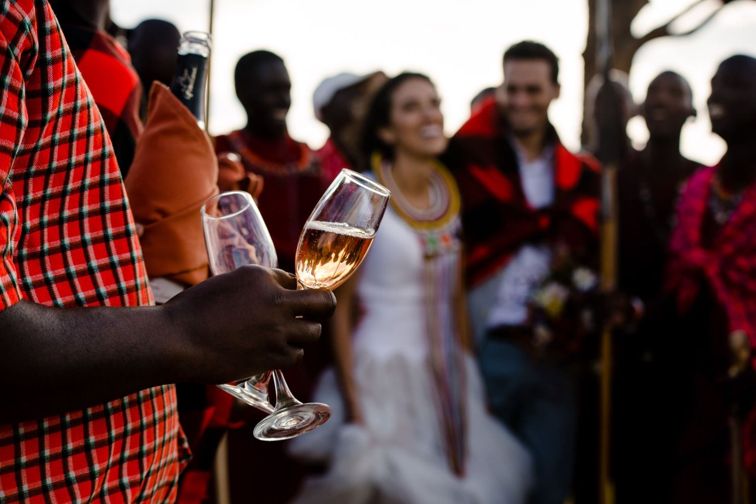 Wedding celebration in traditional African setting with champagne toast in foreground.