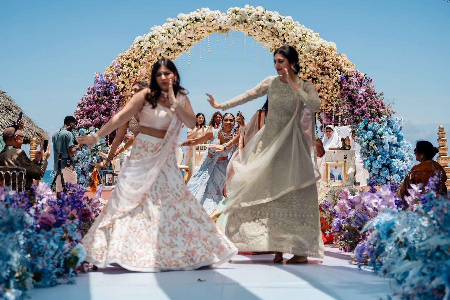 Wedding celebration under floral arch with guests dancing on mirrored platform.