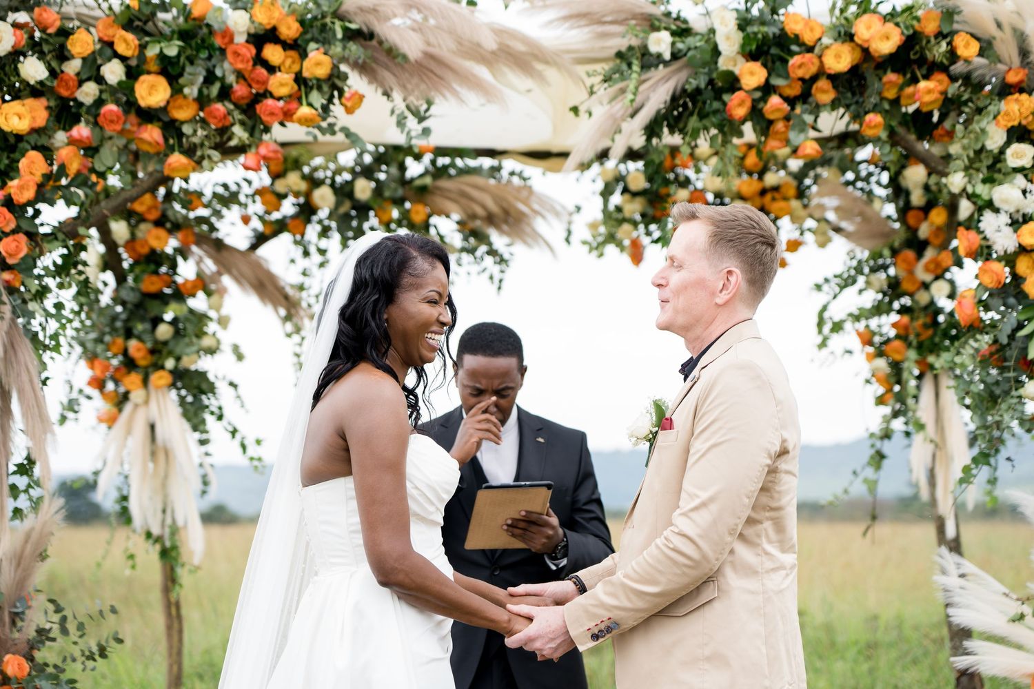 Outdoor wedding ceremony under an arch decorated with orange flowers and greenery.