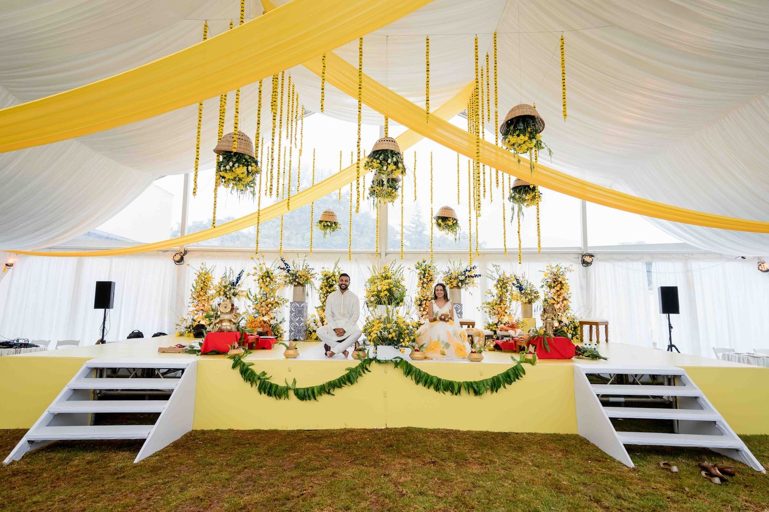 Elegant wedding tent decorated with yellow drapes and hanging floral arrangements.