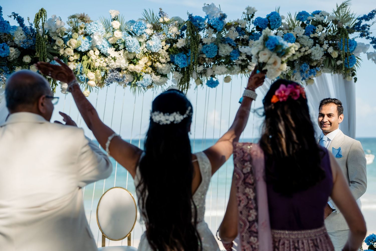 Wedding guests raising hands under floral arch with blue and white decorations.