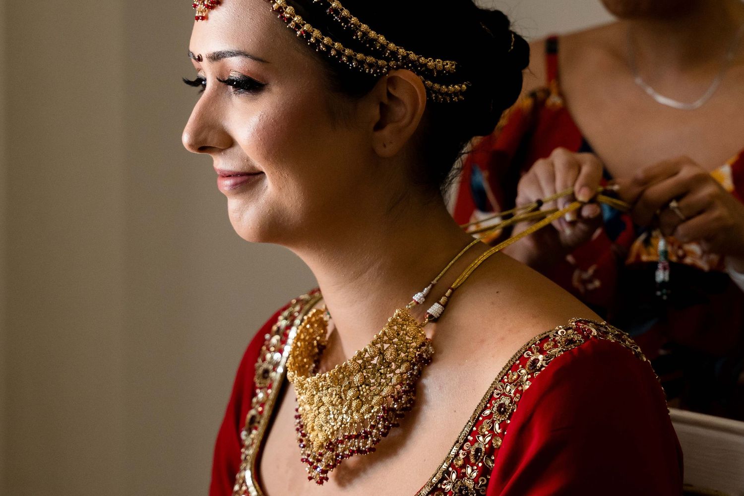 Bride in traditional Indian wedding attire wearing ornate gold jewelry and deep red sari with intricate embroidery details.