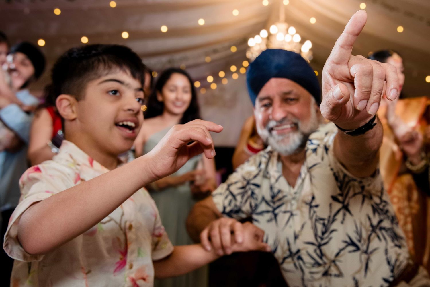 Celebration scene at a wedding reception with partygoers pointing and dancing under string lights.