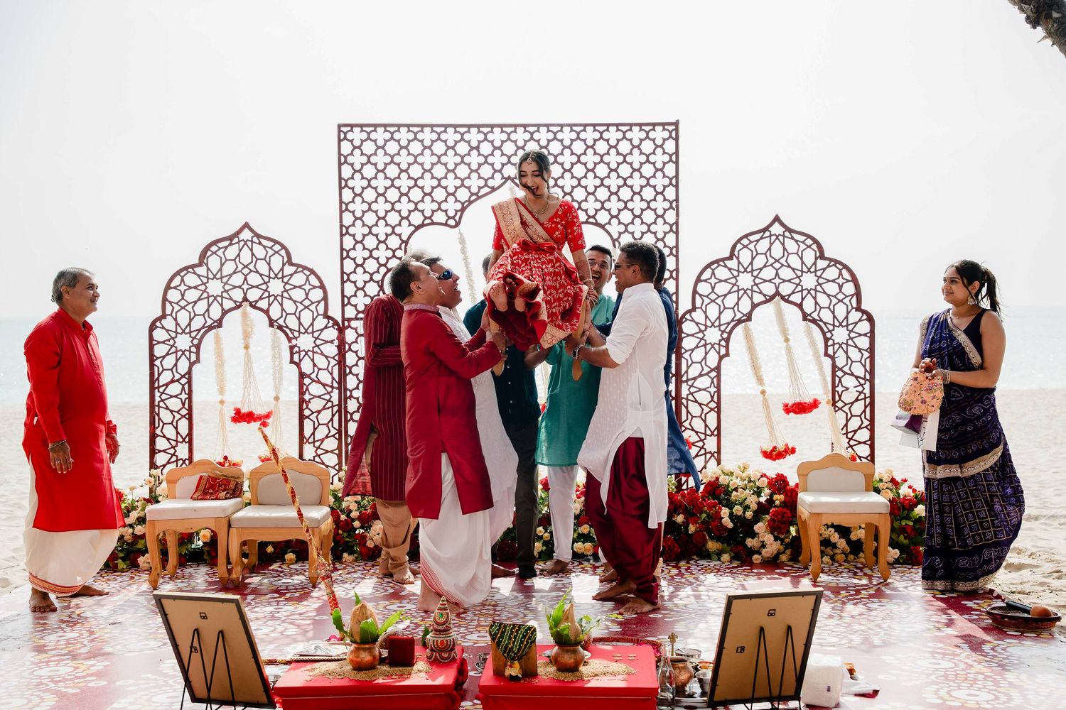 A traditional Indian wedding ceremony setup with ornate white arches and chairs being arranged in sequence.