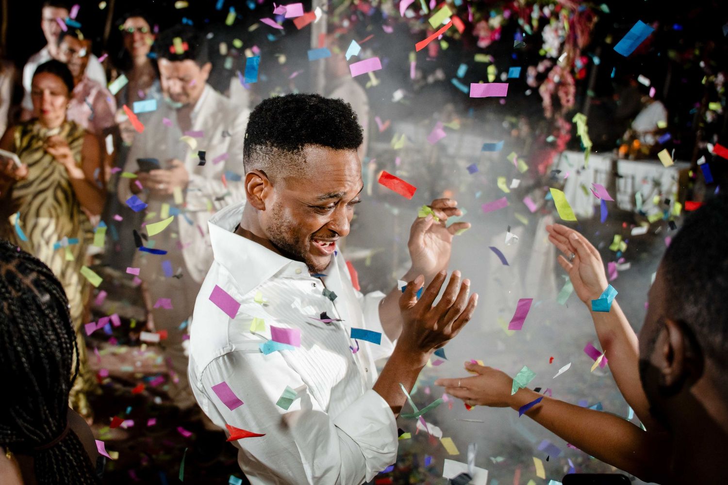 Colorful confetti falls around a couple during a joyful celebration moment in white attire.