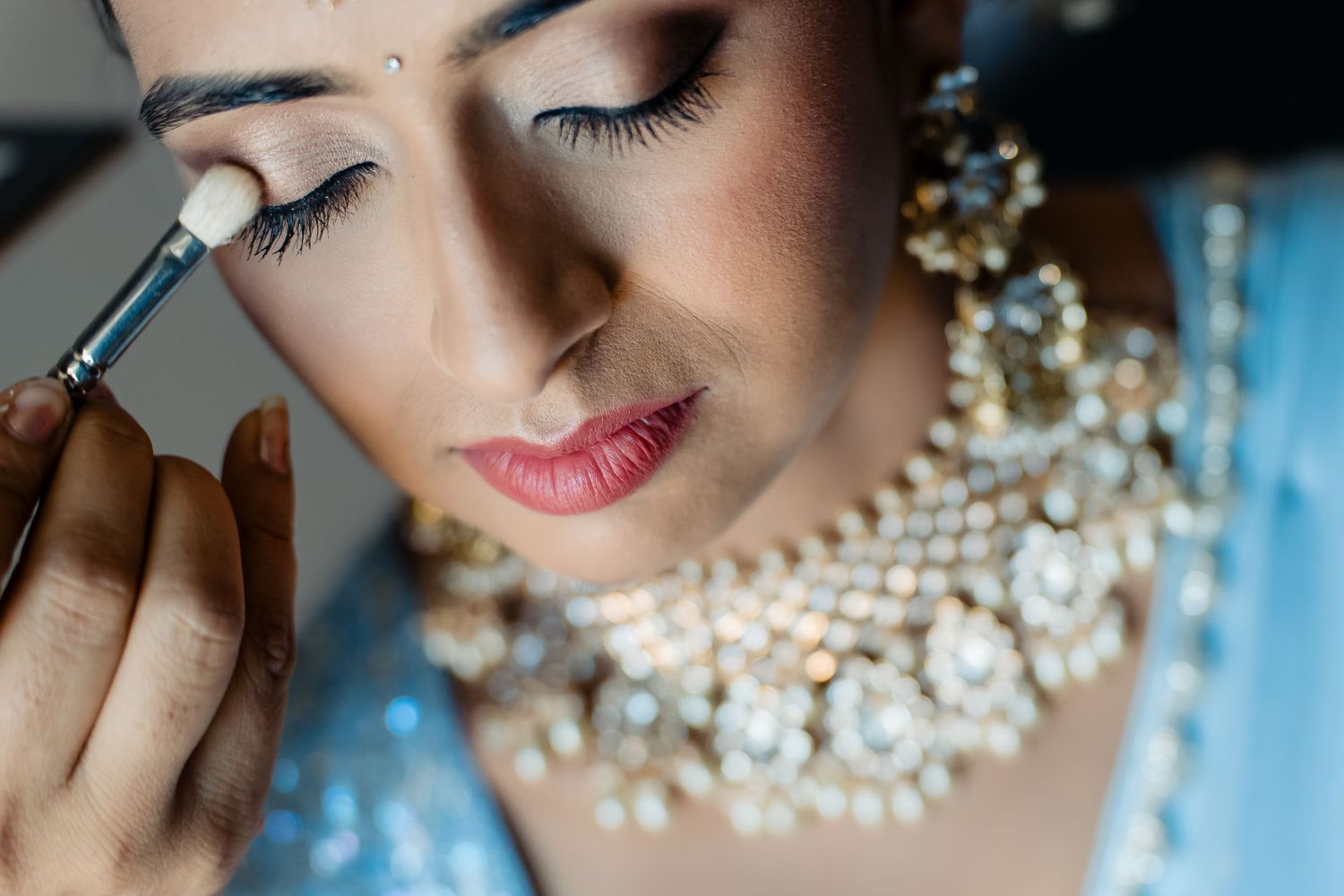 Close-up of bridal makeup application showing pearl necklace and eyeshadow detail.