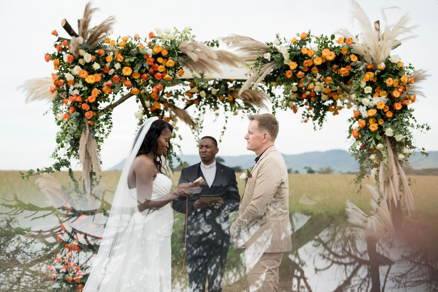 Beautiful outdoor wedding ceremony arch with orange flowers and pampas grass in a field.