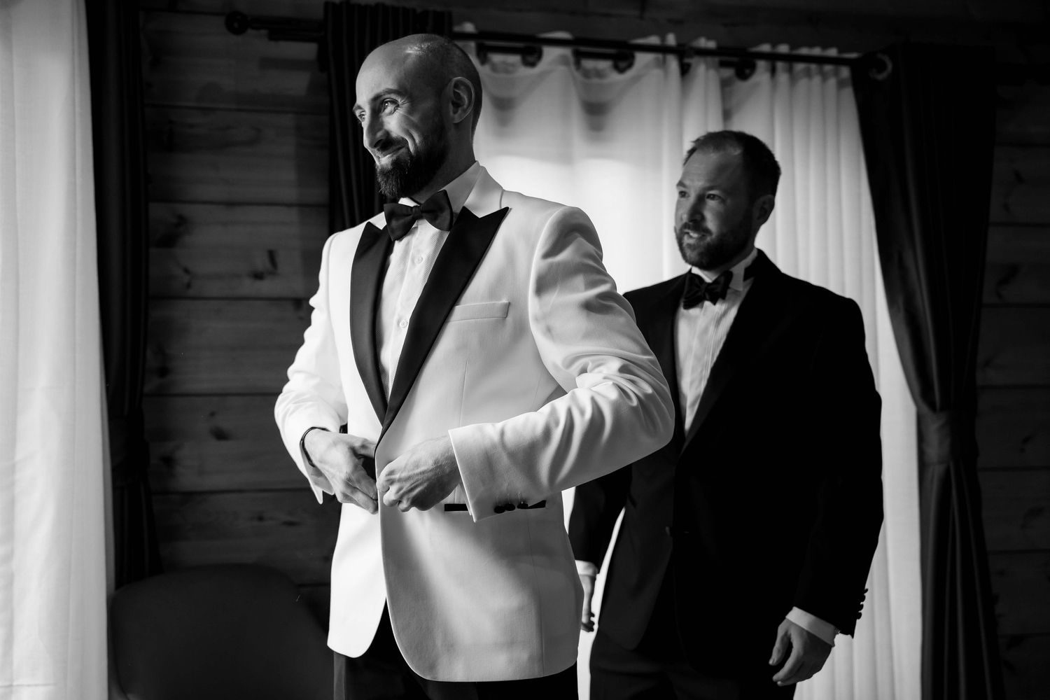 Two men in black and white tuxedos stand together in an elegant black and white photograph.