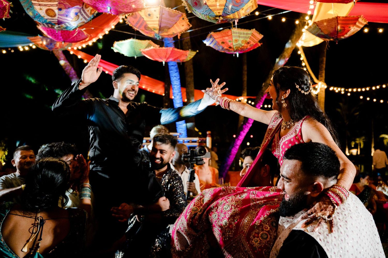 Energetic crowd dancing and celebrating at a nightclub with colorful lighting and decorations overhead.