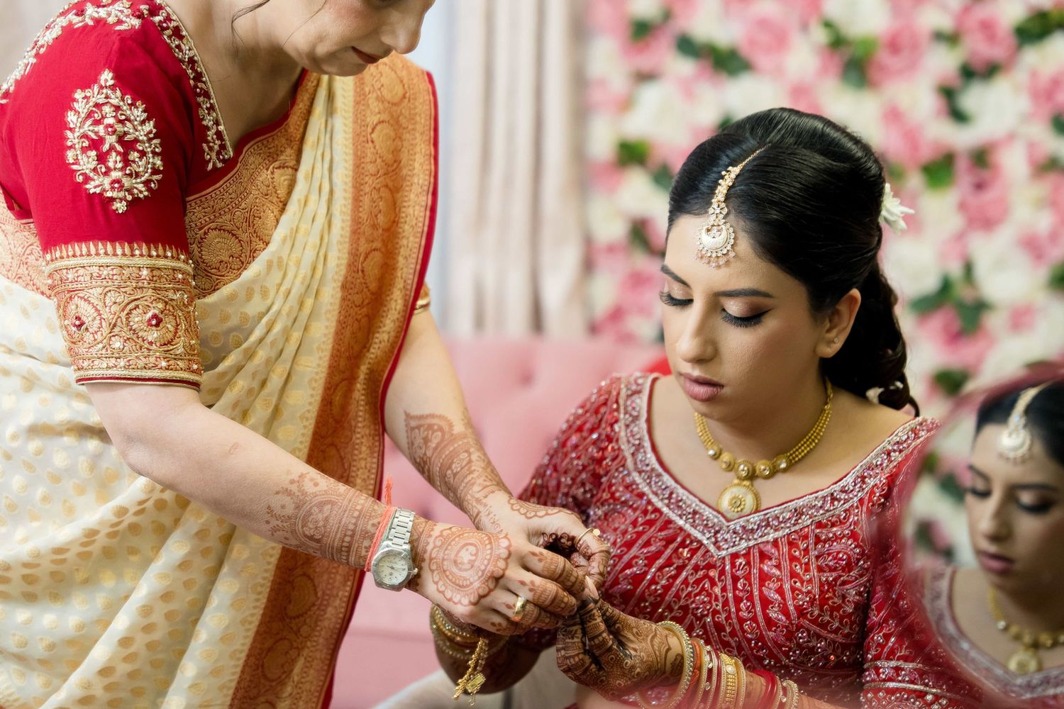 Traditional Indian wedding preparations with detailed red and gold attire and decorative floral backdrop.