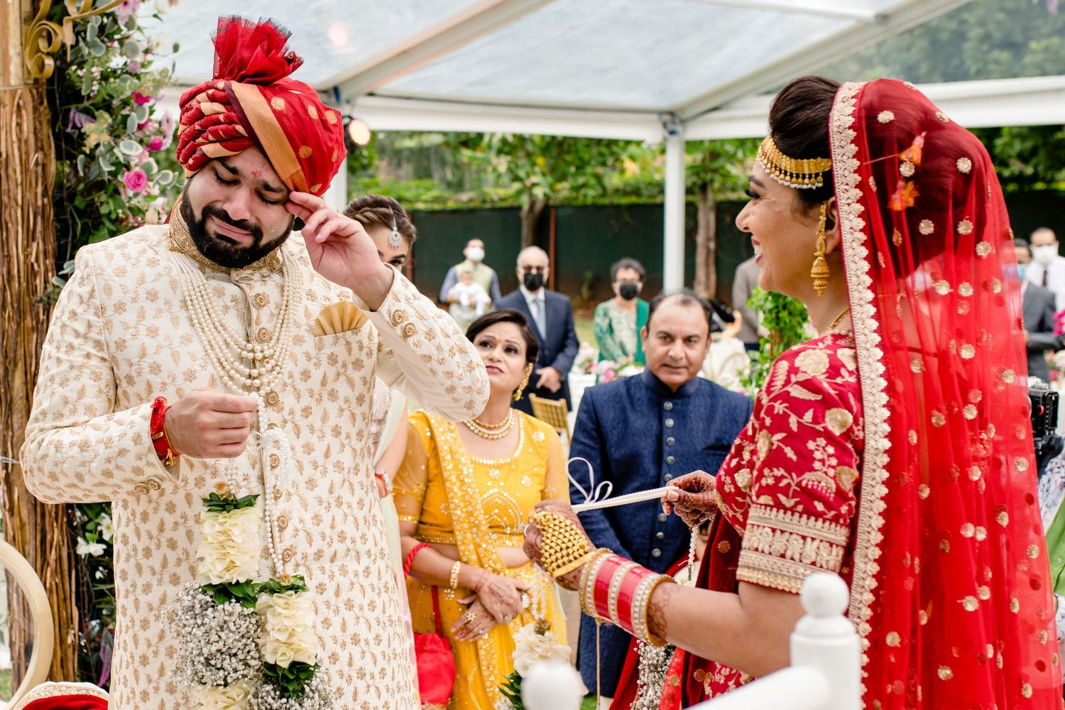 Guests celebrate at a vibrant Indian wedding ceremony with traditional red and gold attire under an outdoor canopy.