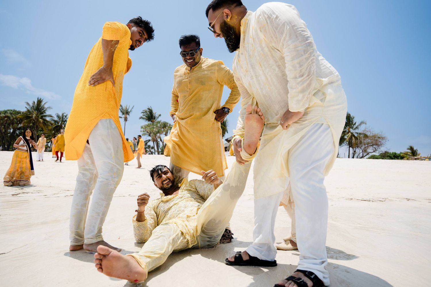 A group in coordinated yellow and white outfits poses together on a sunny beach for photos.