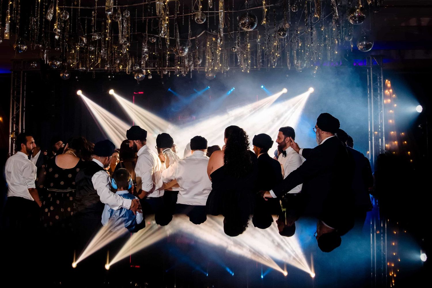 Silhouettes of party guests beneath dramatic ceiling lighting and hanging decorations.
