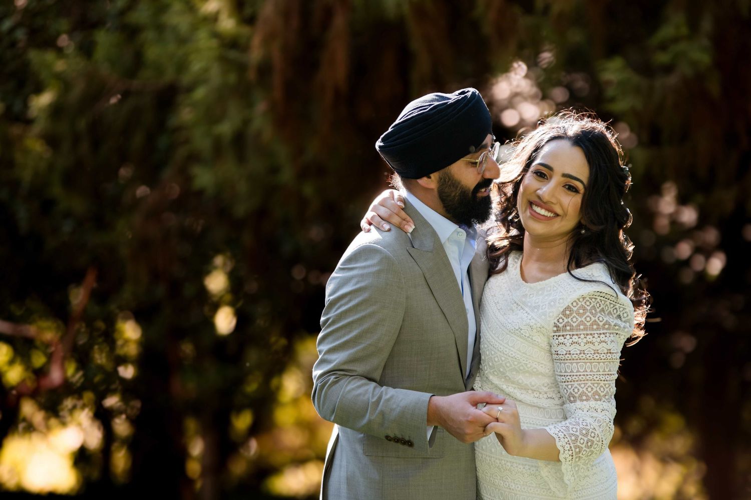 A couple shares a joyful moment in traditional wedding attire against a natural backdrop.