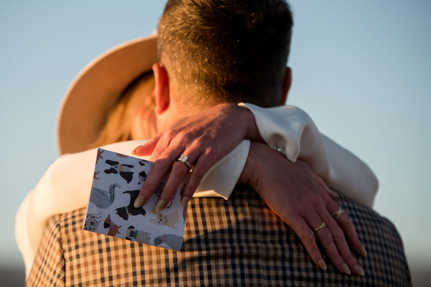 Close up of hands embracing showing wedding rings against a blue sky background.