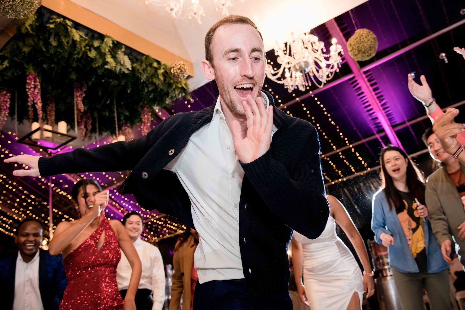 Energetic celebration captured at wedding reception with purple lighting and chandelier.