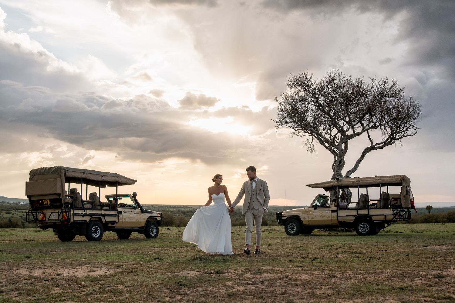 Safari vehicles silhouetted against dramatic sunset sky during wedding photoshoot.