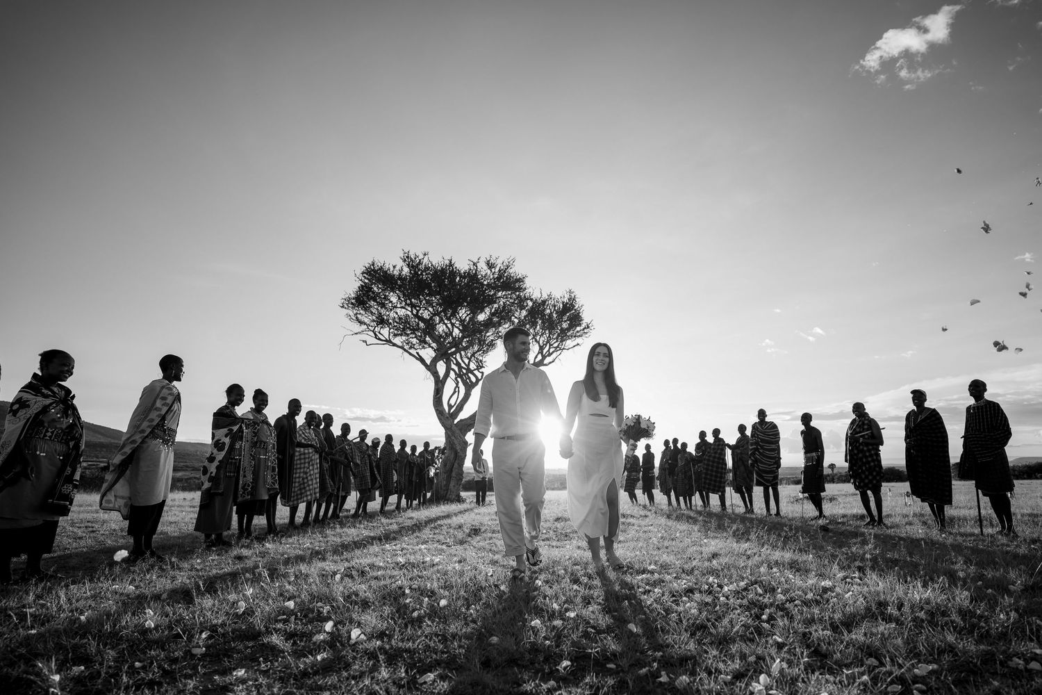 A black and white silhouette of a wedding ceremony with guests lined up against a dramatic sky.