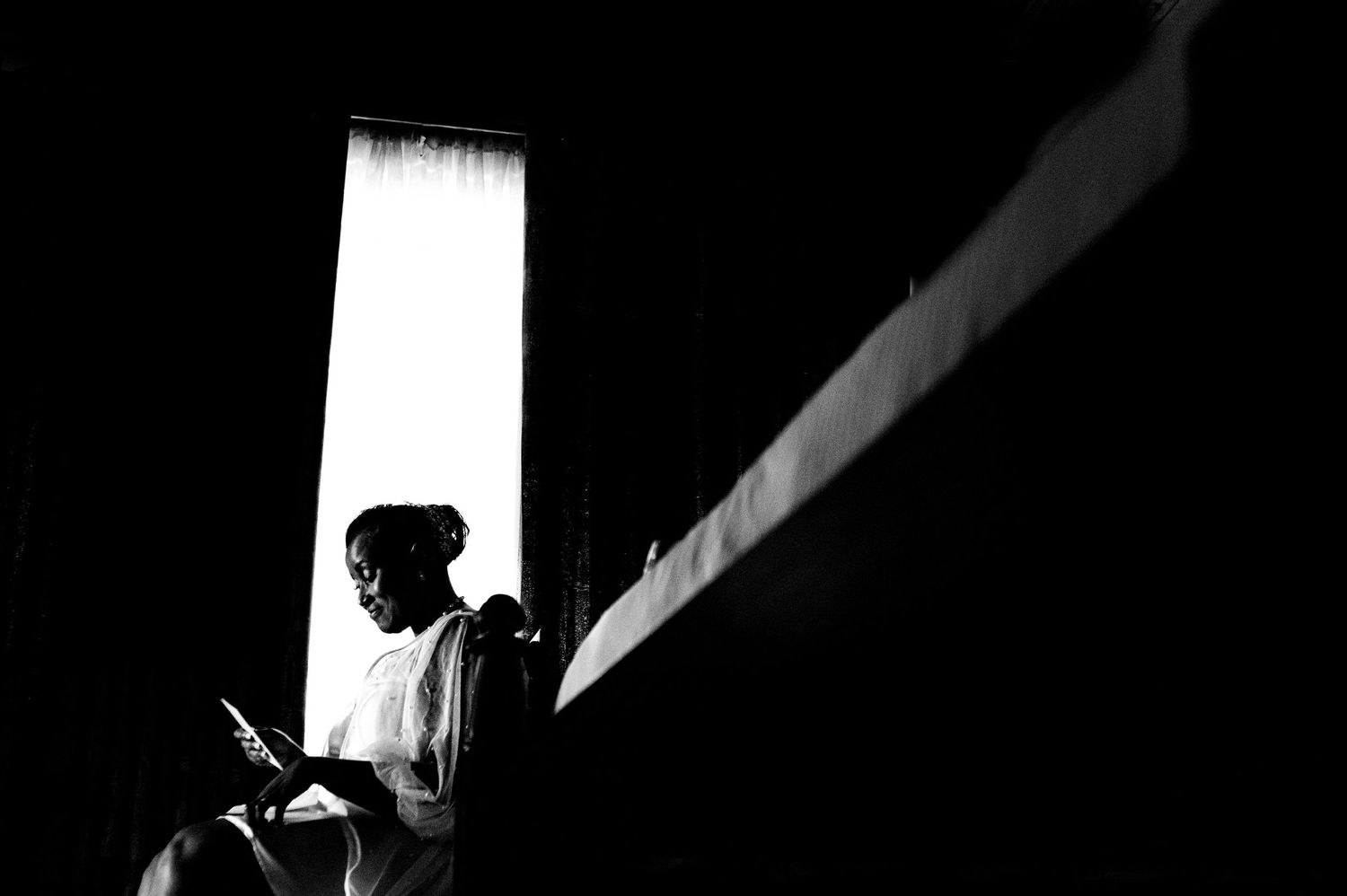Dramatic black and white silhouette of a bride getting ready by a window with flowing veil and dress.