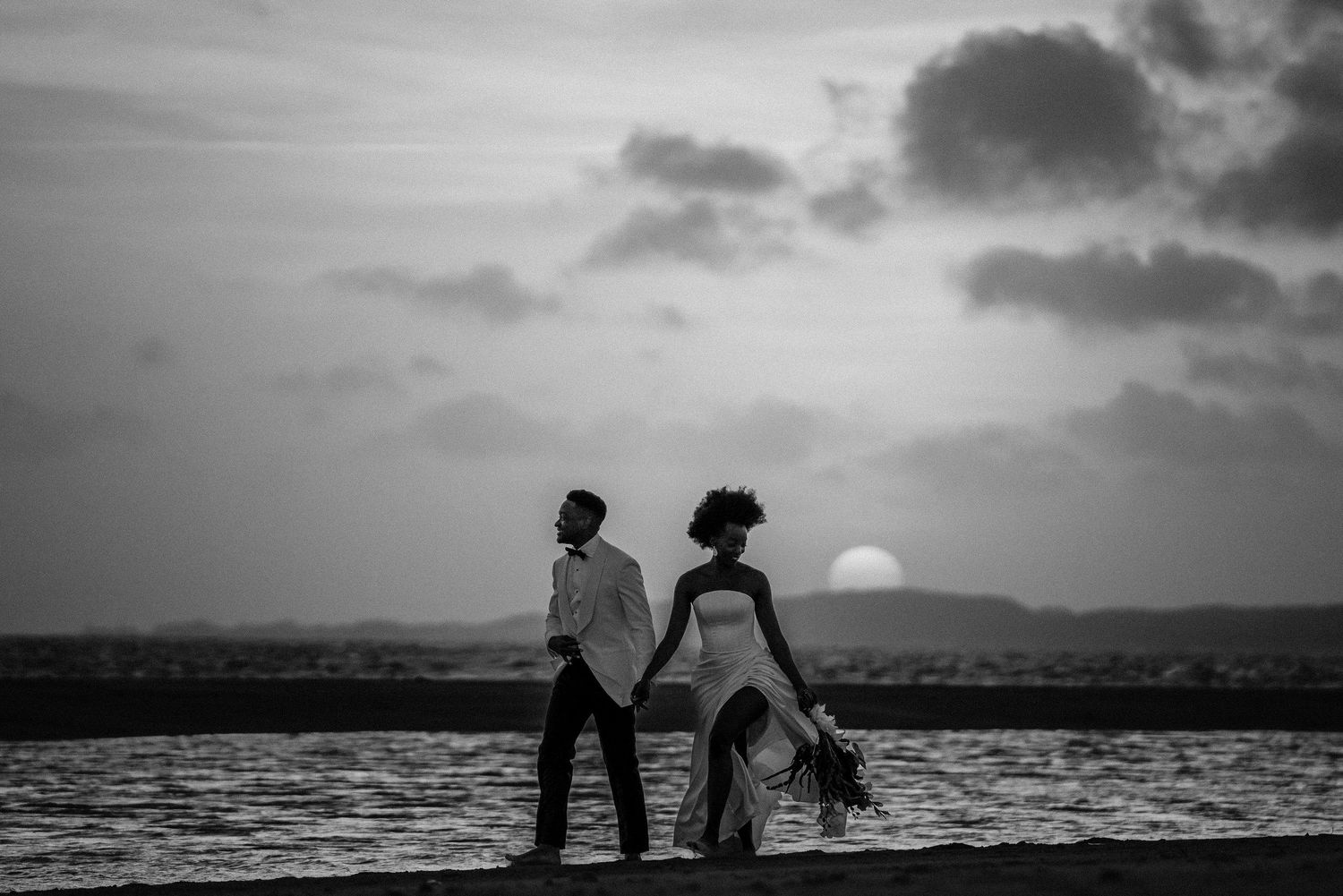 Silhouettes of couple walking on beach at sunset after their Kenyan wedding in Lamu