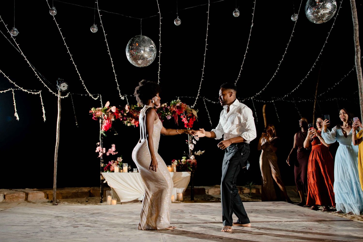 Wedding guests dance under sparkling disco balls and string lights at an evening reception celebration.