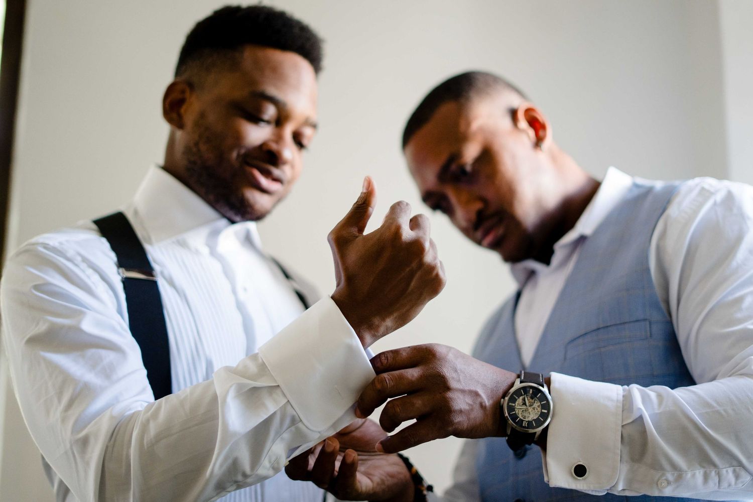 Groomsmen help each other put on cufflinks and adjust formal attire while getting ready for a wedding.