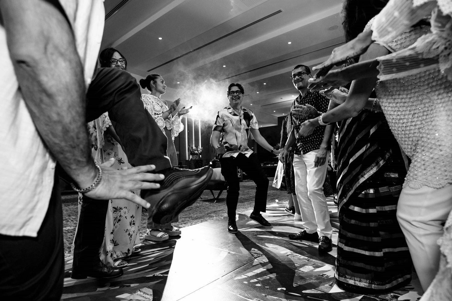 Black and white photo of people dancing energetically on a dance floor with a flash of light in the background.