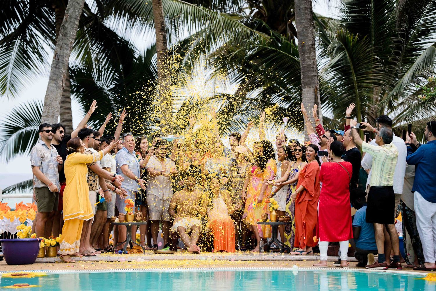 Wedding guests celebrate with sparklers under palm trees at a tropical beach reception during sunset.