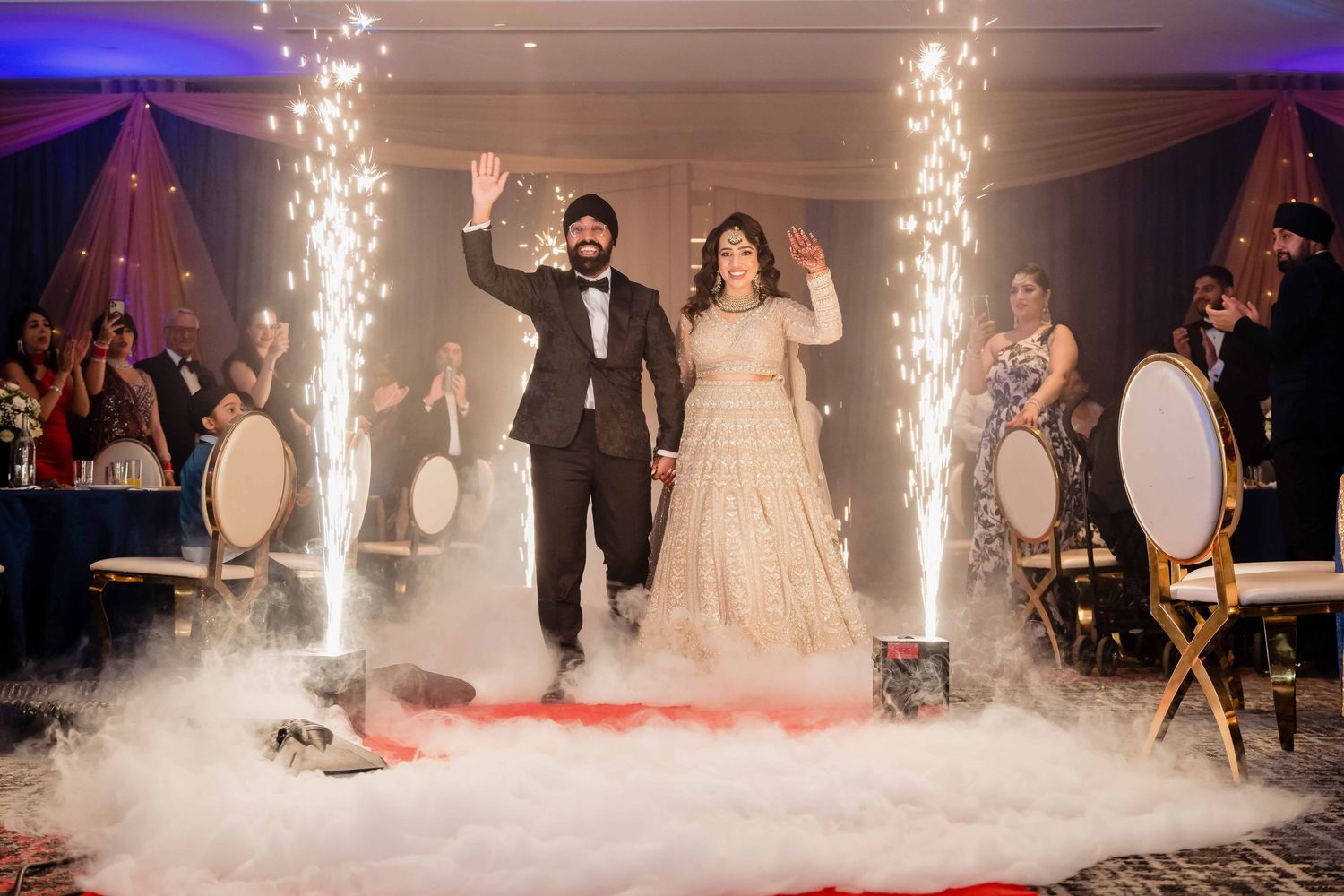 A couple makes their grand entrance at a wedding reception with sparklers and fog effects on a red carpet.