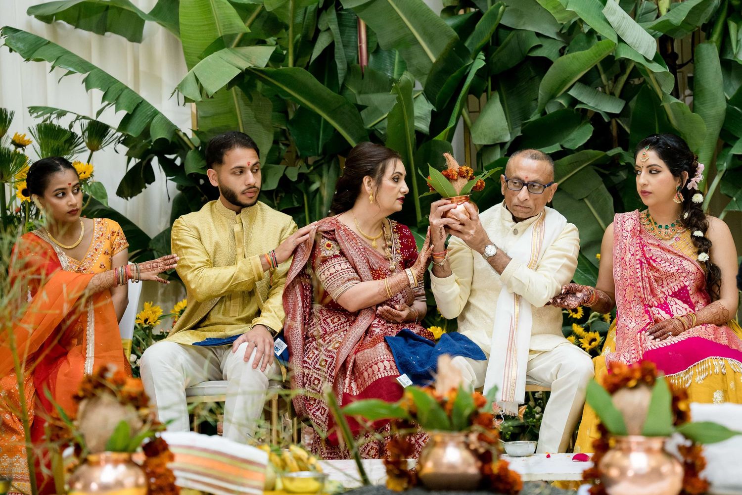 Guests in colorful traditional Indian attire participating in a ceremonial ritual with flowers and offerings.