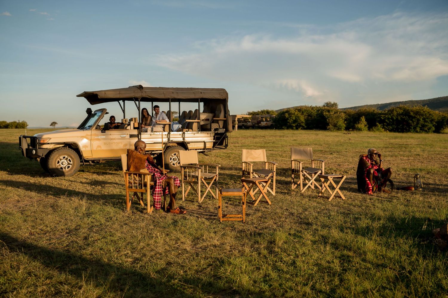 Safari vehicle and camping chairs set up for sunset viewing in African wilderness.