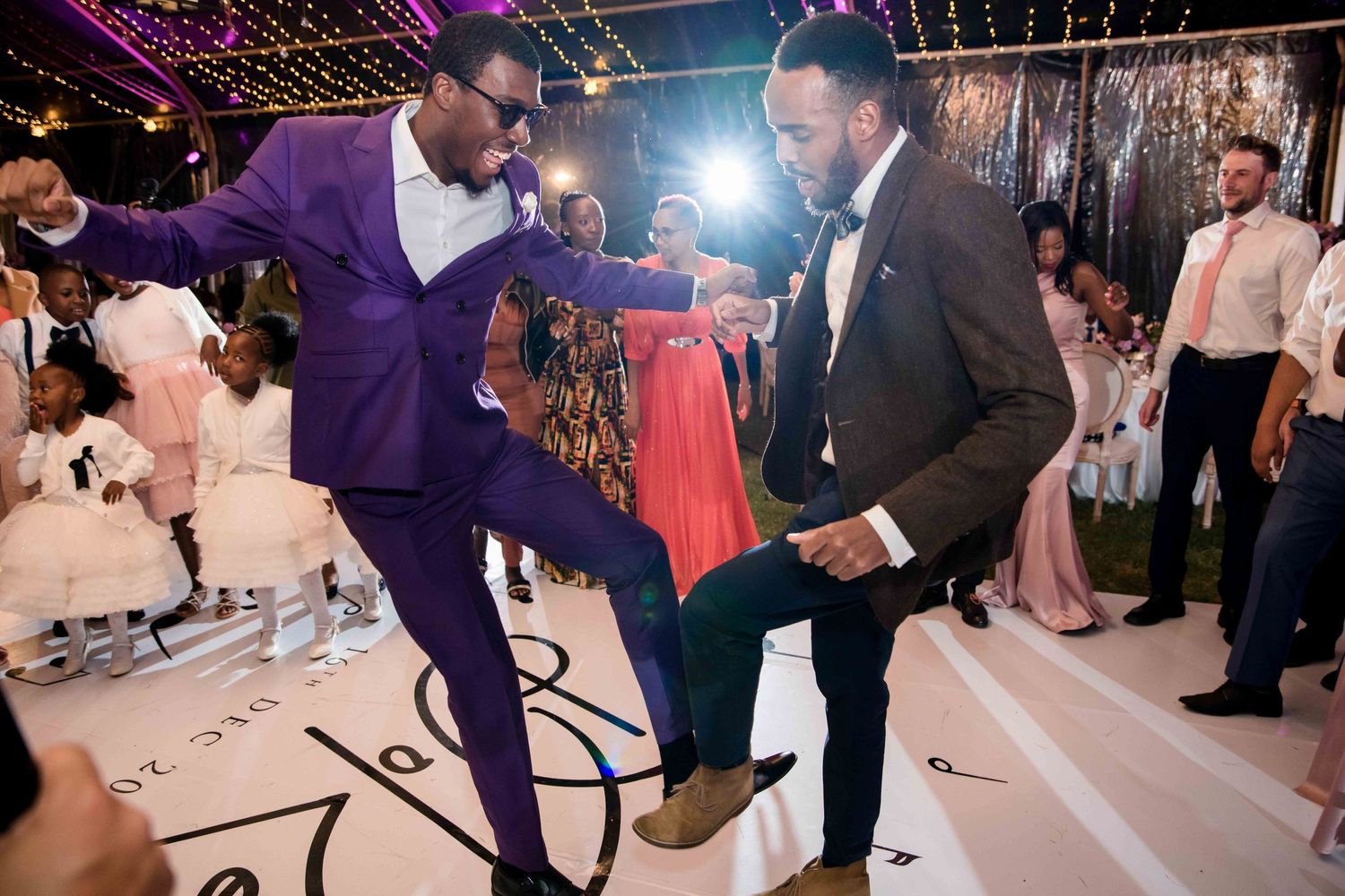 Two wedding guests dance energetically on a decorated dance floor during a reception celebration.