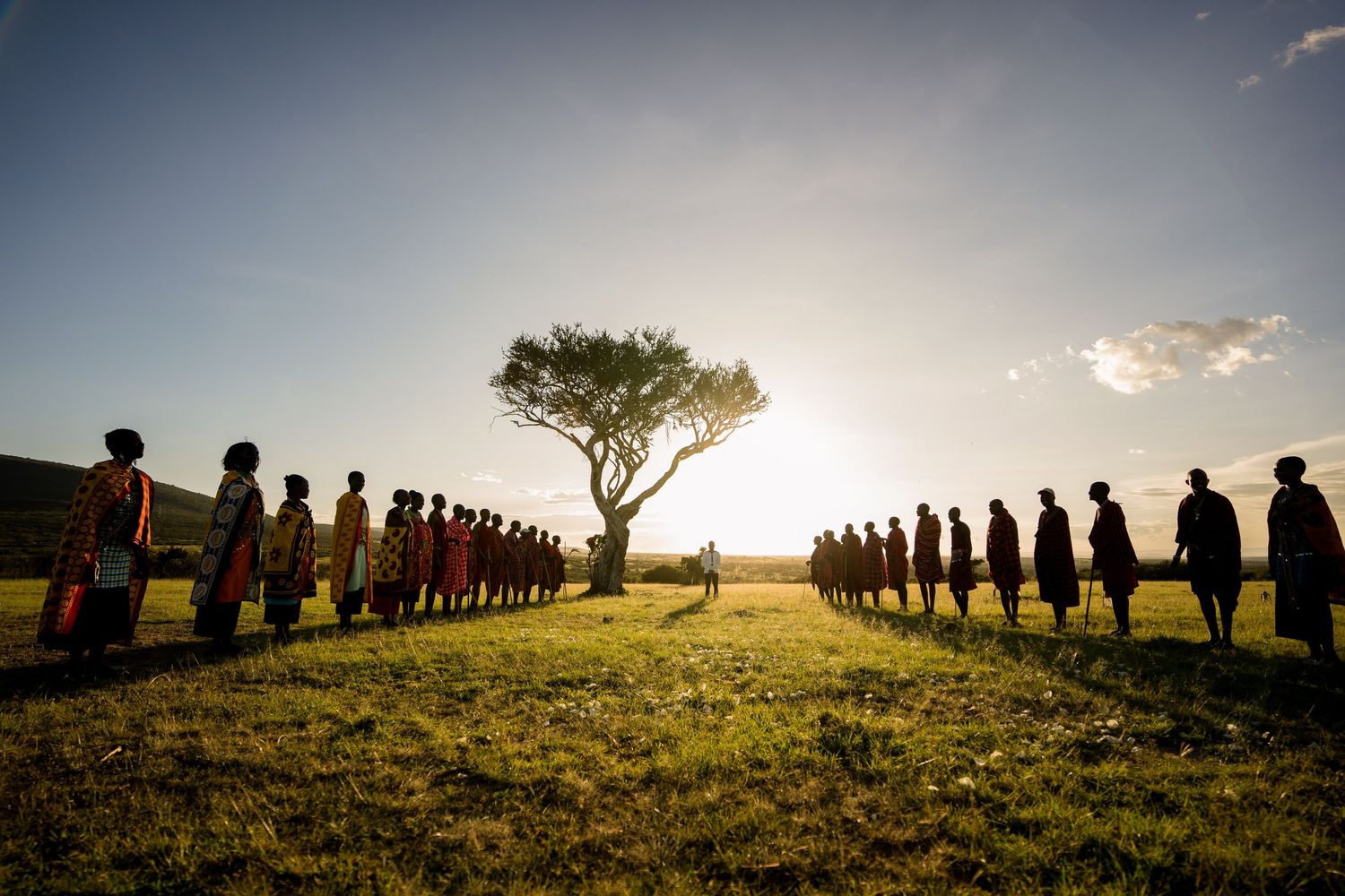 Silhouettes of people gathered around a lone tree at sunset in African savanna.