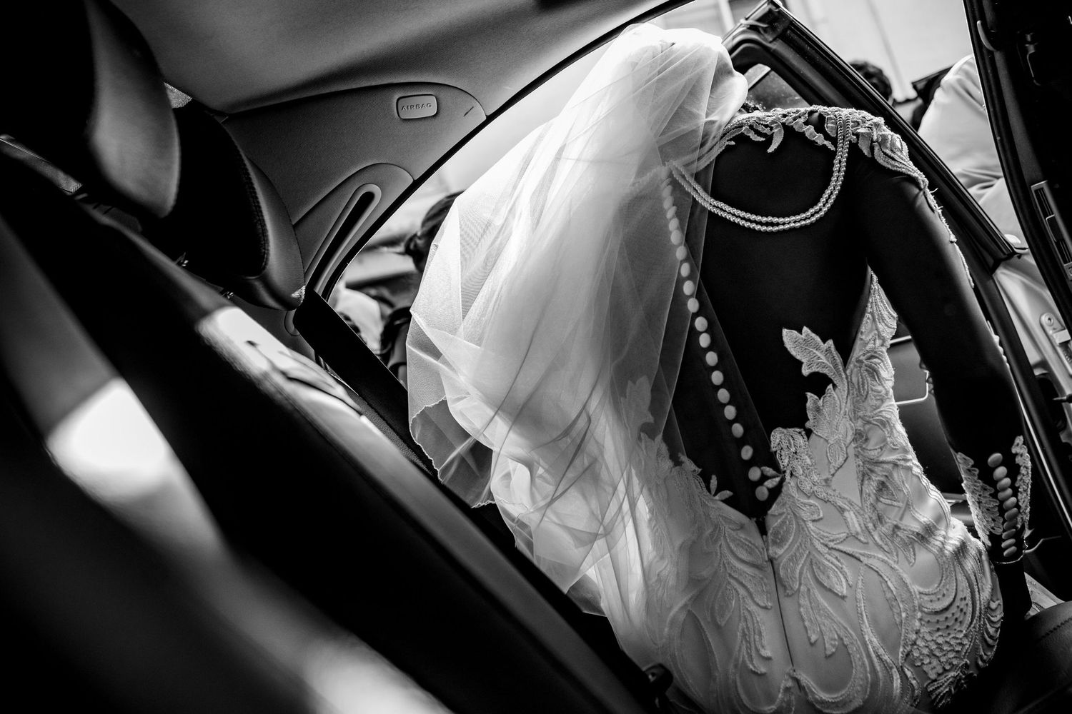 Black and white detail of a wedding dress laid across a car seat.